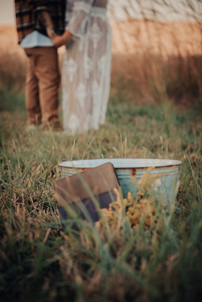 couple standing in a field, all you see is their legs in the background, and a bucket in the focus
